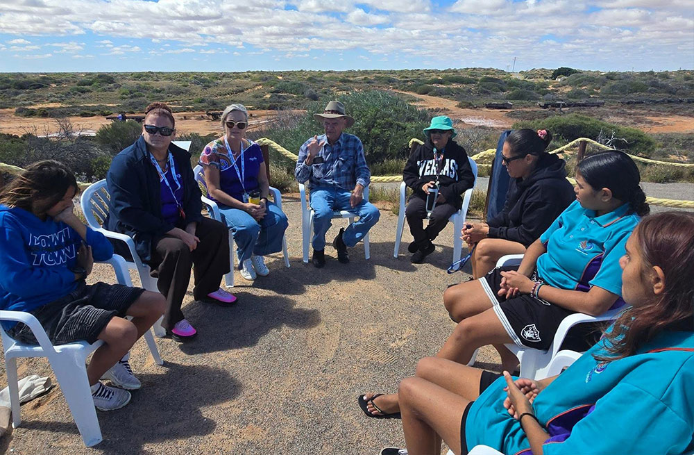 Participants of the Bush Classrooms sitting in a yarning circle with the bush landscape on the horizon