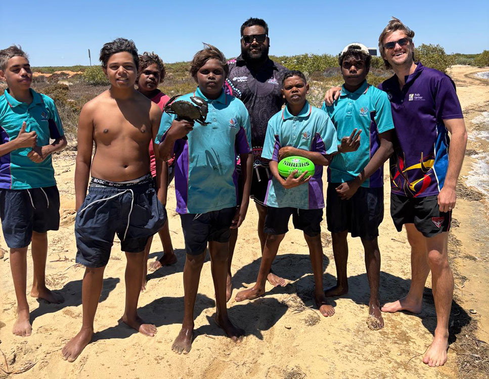 Participants of the Bush Classrooms posing for the camera, barefoot on the sandy shore