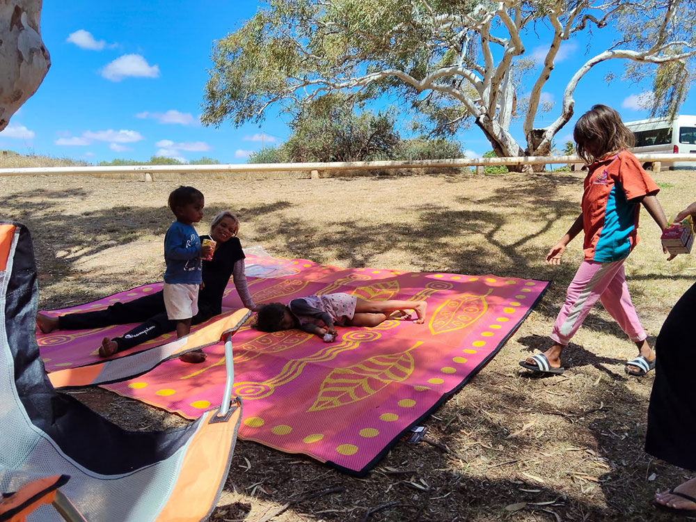 Kids and mother playing on a canvas mat laid over the grass under the shade of a gum tree