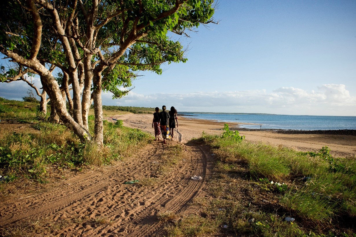 Three indigenous women walk along a bush track to the beach