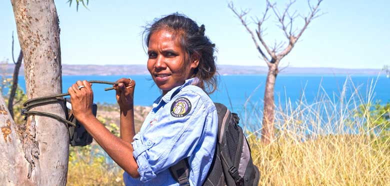 An Indigenous Ranger, Azamia Malay, attaching a motion sensor camera to a tree near water