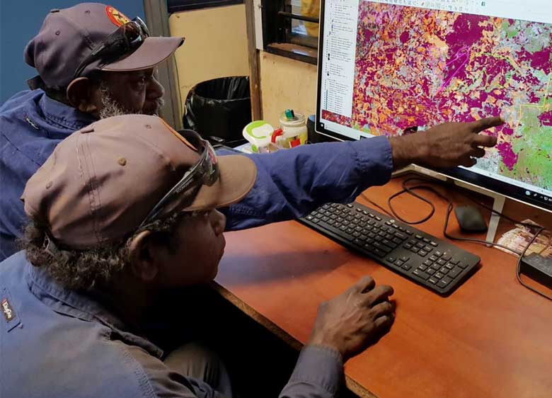 Two Indigenous rangers sitting at a computer pointing at a fire management planning map
