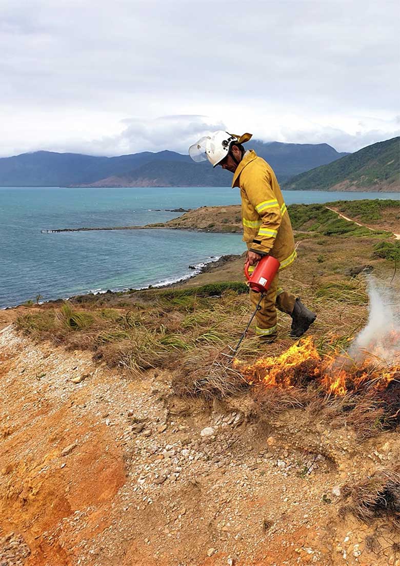 Yuku Baja Muliku Land and Sea Ranger, Gauai Wallace, undertaking cultural burning at Archer Point with the coastline in the background