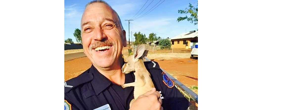First Class Constable Shane Bianchard smiling with a joey kangaroo in his arms 