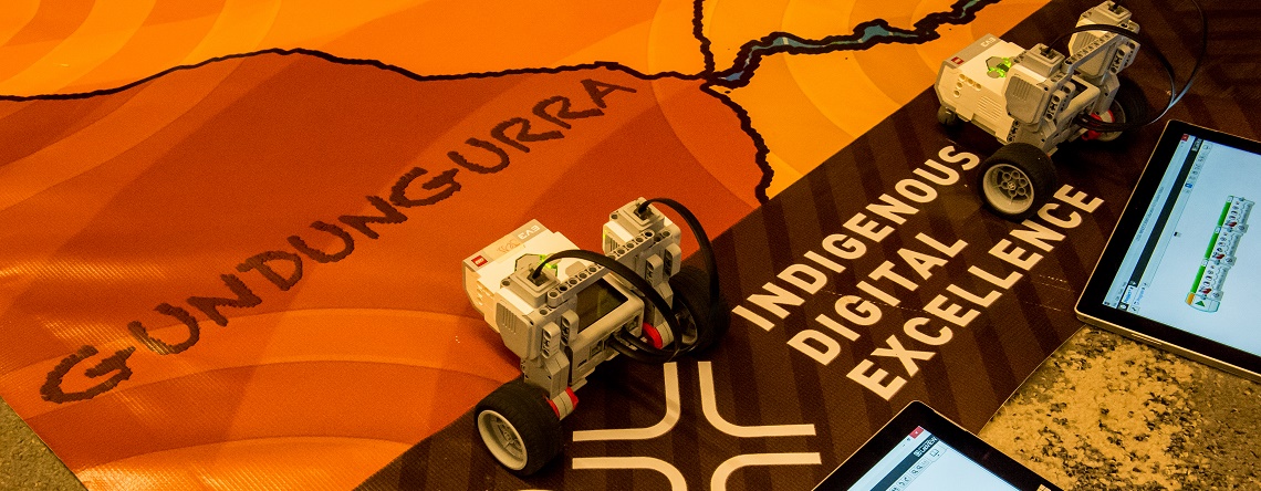 Indigenous Digital Excellence Flint Programme banner on the ground with robot type machines sitting on it