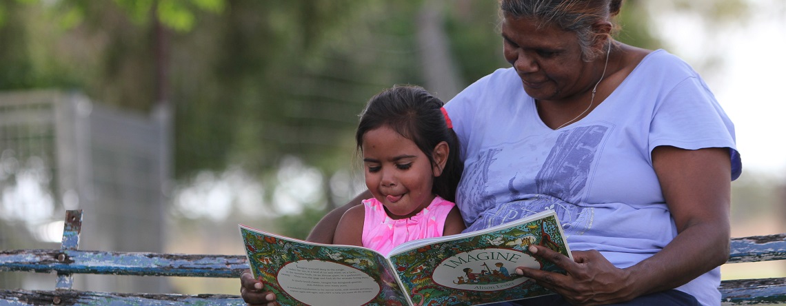 Indigenous woman and child sitting on a park bench reading a book