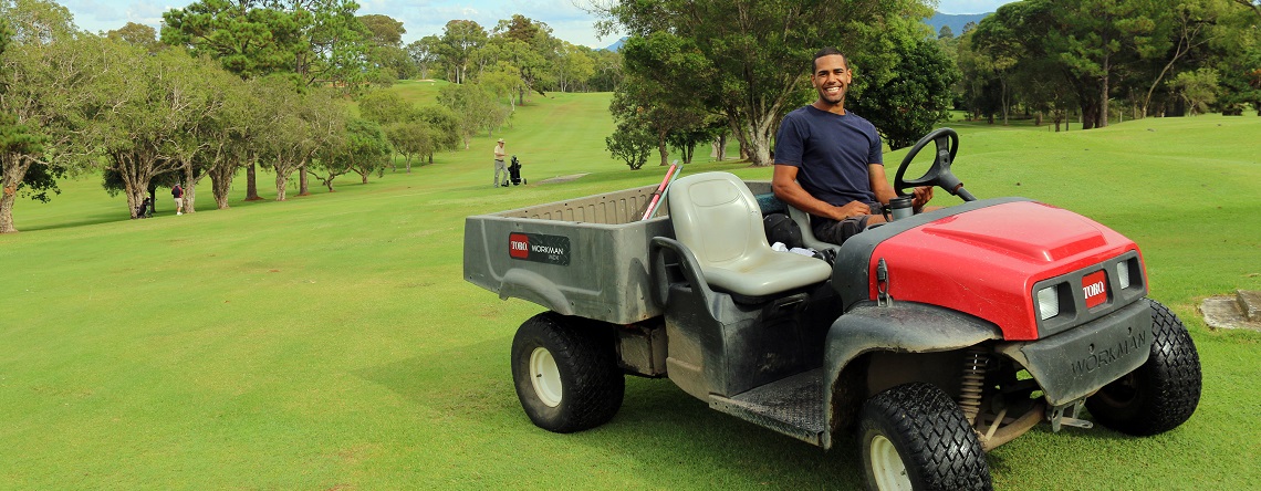 Indigenous man sitting on lawn mower smiling, at a golf course