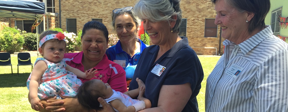 Members and participants of the Armidale Aboriginal Mothers and Babies Program smiling at a baby in a members arms