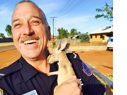 First Class Constable Shane Bianchard smiling with a joey kangaroo in his arms 