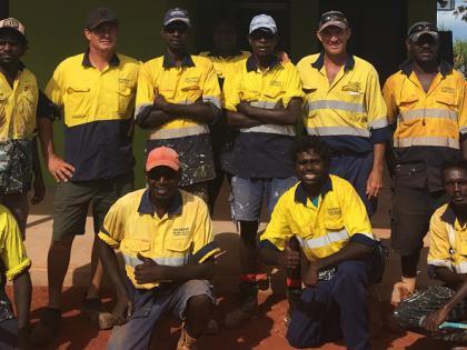 A group of Indigenous men in safety clothing looking at the camera, some standing in a line, others crouched in front