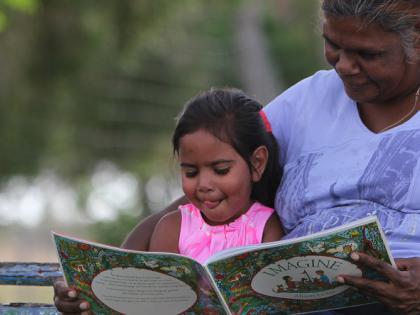 Indigenous woman and child sitting on a park bench reading a book