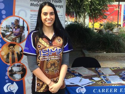 Indigenous student smiling and standing in front of Indigenous Youth Mobility Pathways banner
