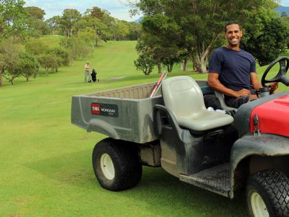 Indigenous man sitting on lawn mower smiling, at a golf course