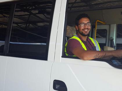 Indigenous man sitting in a white van with Action Buses logo on the side