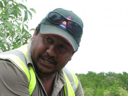 Indigenous man crouching down with a stick in his hand, a river in the background