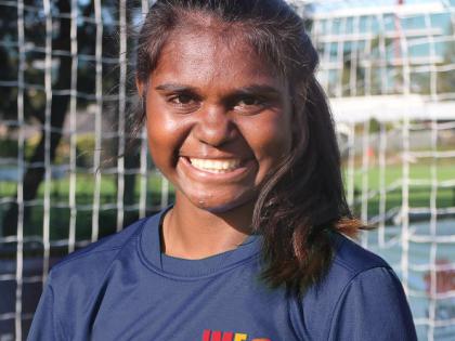 Indigenous girl smiling, standing in front of a soccer goal