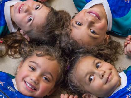 Four smiling indigenous girls lying on the floor in a circle, linking hands