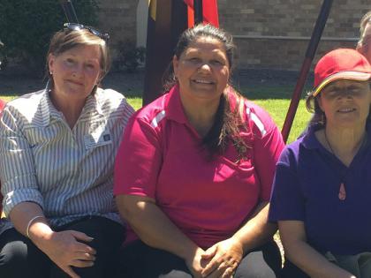 Five women sitting outside smiling at the camera, in front of the ATSI and Australian flags