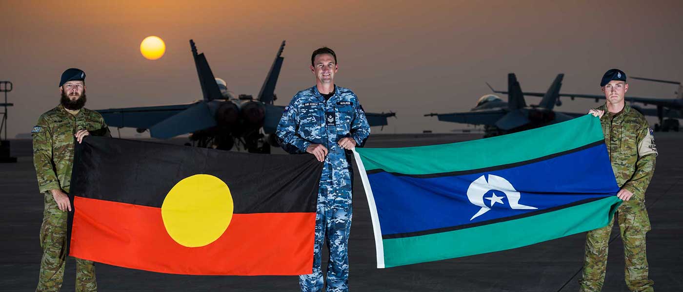 Leading Aircraftmen Brent Irvine, left, and Jackson Saddler, right, proudly display the Aboriginal and Torres Strait Islander flags with Flight Sergeant Luke Walker