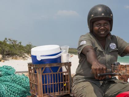 This photo shows Dhimirru Ranger, Rakrakpuy Marika, on a white beach riding a quad bike and towing a trailer. 