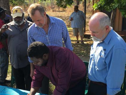 This photo shows Minister for Indigenous Affairs Nigel Scullion and the Executive Director of the Office of Township Leasing, Greg Roche looking on as Trustee of the Tiwi Aboriginal Lands Trust, Kim Puruntatameri, signs a township lease covering Pirlangimpi.