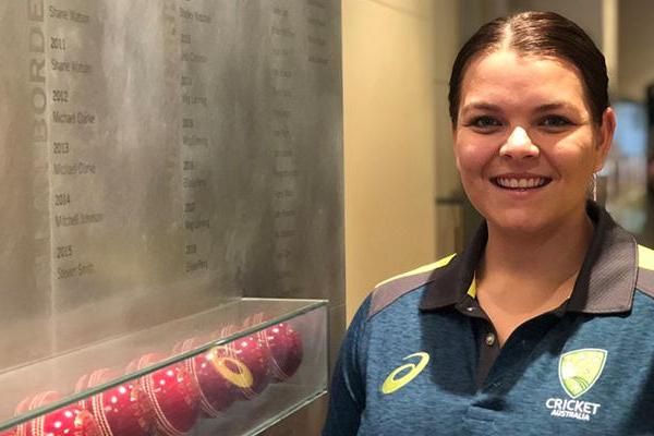 Image of Courtney Hagen. She is smiling while standing next to a memorial cricket wall.