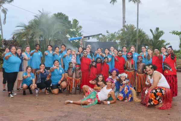 Group of people standing together pointing towards the camera. There are some people in traditional Indigenous ceremonial dress.