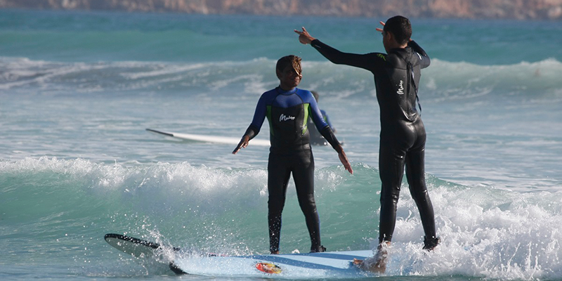 Two indigenous youths surfing on a beach