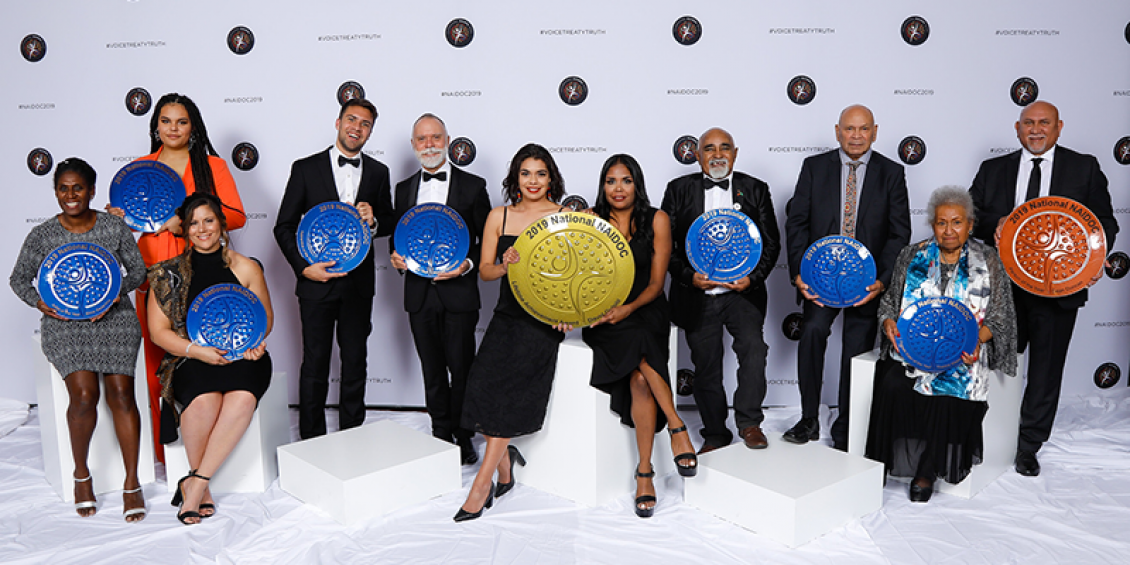 A group of 11 men and women in a row, they each hold an award. 