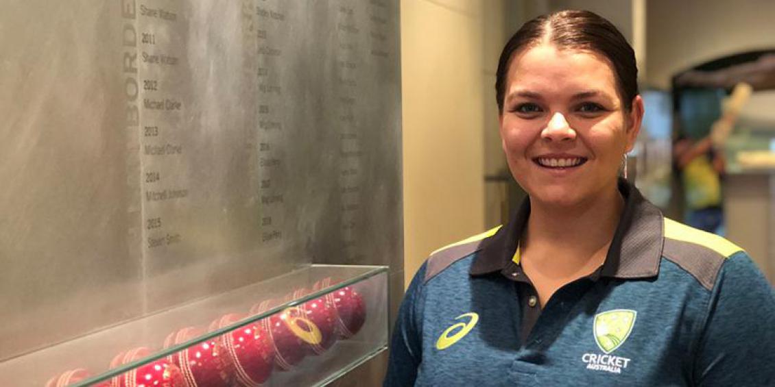 Image of Courtney Hagen. She is smiling while standing next to a memorial cricket wall.